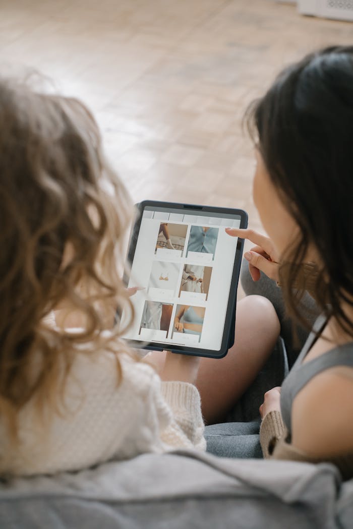 Two women sitting together, shopping online using a tablet, sharing ideas and browsing products.